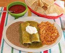 Two beef burritos with green sauce, sour cream, refried beans, and rice